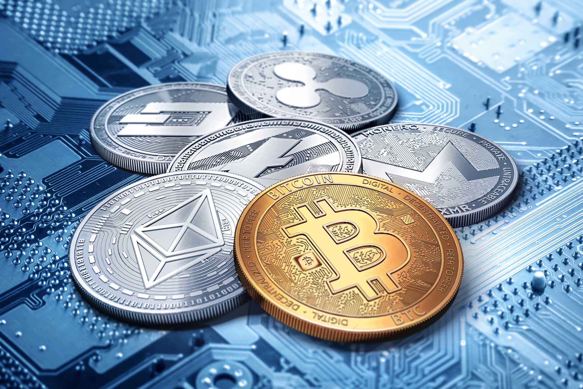 Several physical coins representing different cryptocurrencies, including Bitcoin, Ethereum, Litecoin, Ripple, and Monero, are displayed on top of a blue circuit board background.