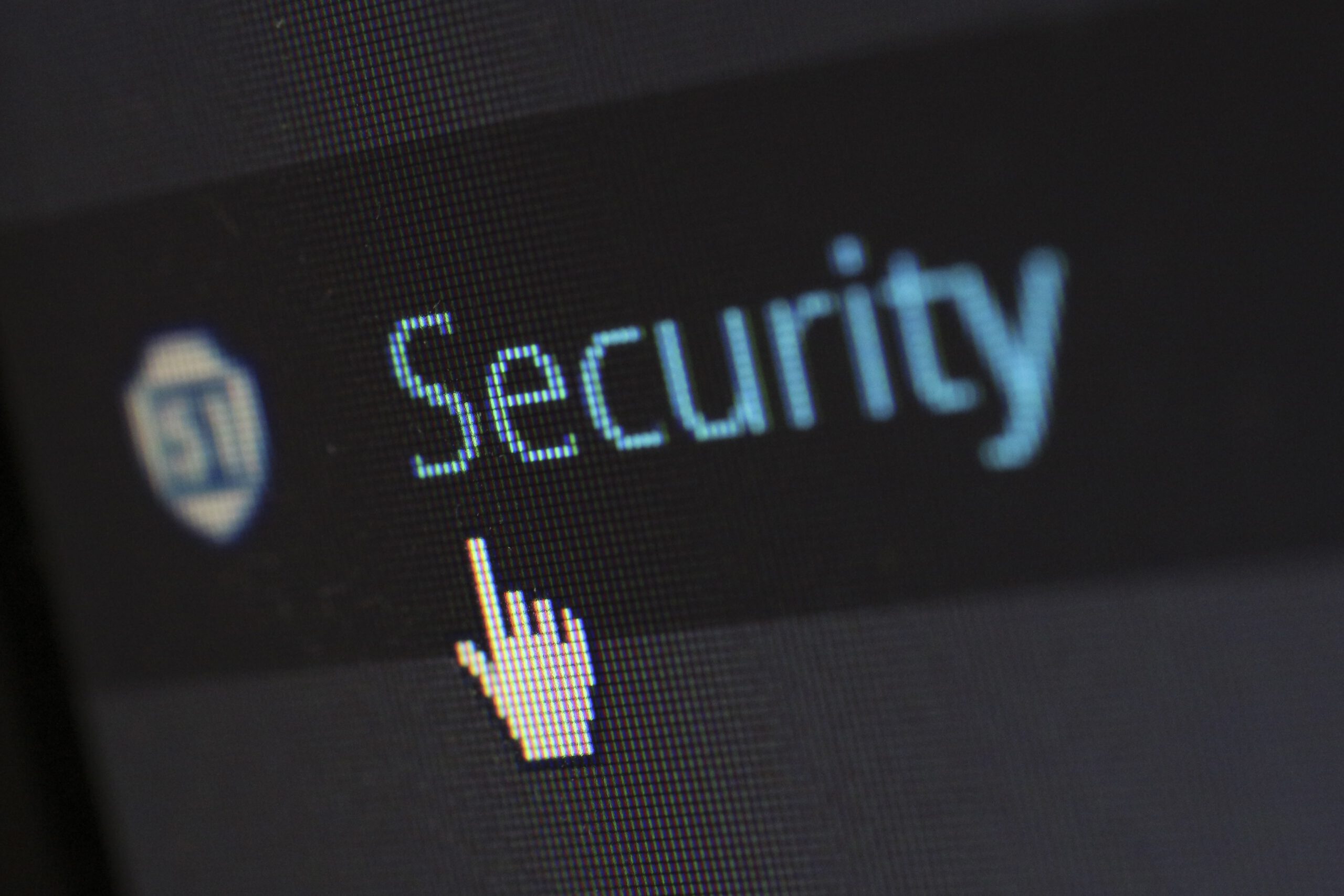 A computer screen displays the word Security in blue text with a pixelated hand cursor pointing at it, symbolizing cybersecurity or online security.