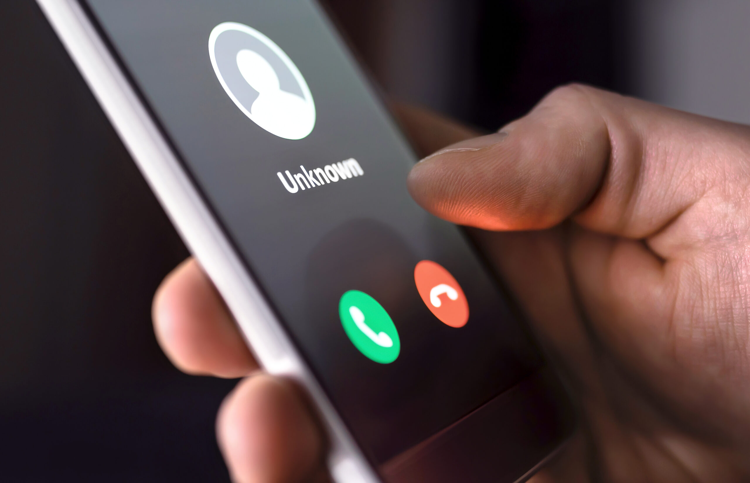 A hand holding a smartphone displaying an incoming call from an unknown caller, with green and red buttons to accept or decline the call.
