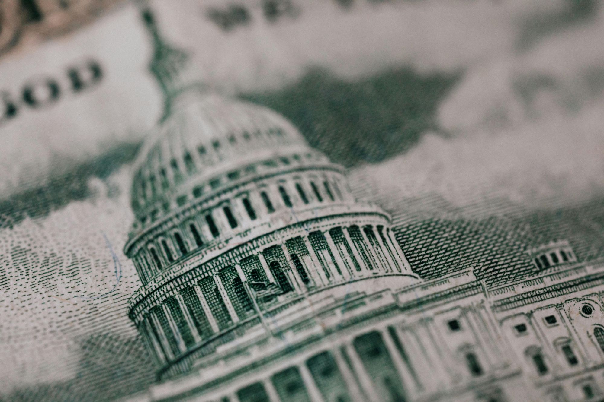 Close-up image of the U.S. Capitol building printed on paper currency, showing detailed engraving lines and architectural features in shades of green and gray.