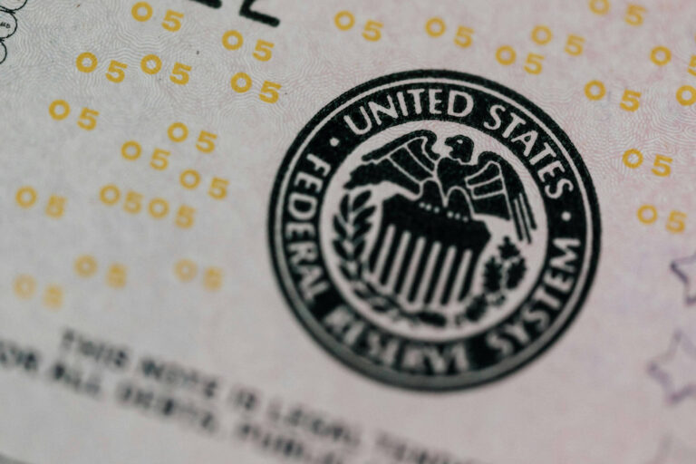 Close-up of the United States Federal Reserve System seal printed on paper, with yellow security numbers and fine text visible in the background.