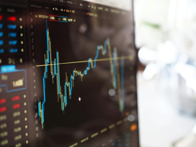 A close-up of a computer screen displaying a financial chart with blue and yellow candlestick graphs, price data, and numbers, indicating stock market activity and trading analysis.
