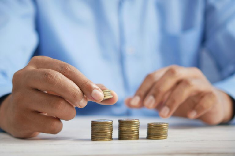A person wearing a blue shirt is stacking coins into neat piles on a light-colored table, focusing on organizing the money with both hands.