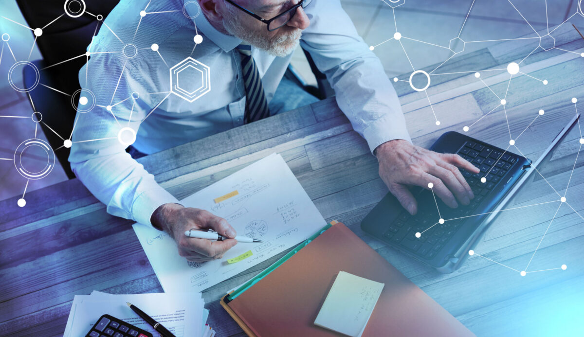 Mature business professional working with financial documents and a laptop, with a digital network overlay representing AI and information security.