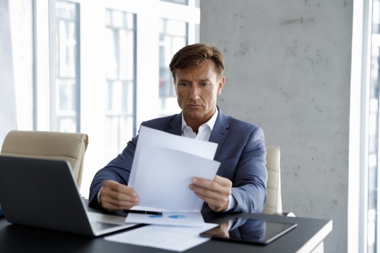 Corporate executive reviewing severance package documents at his office desk