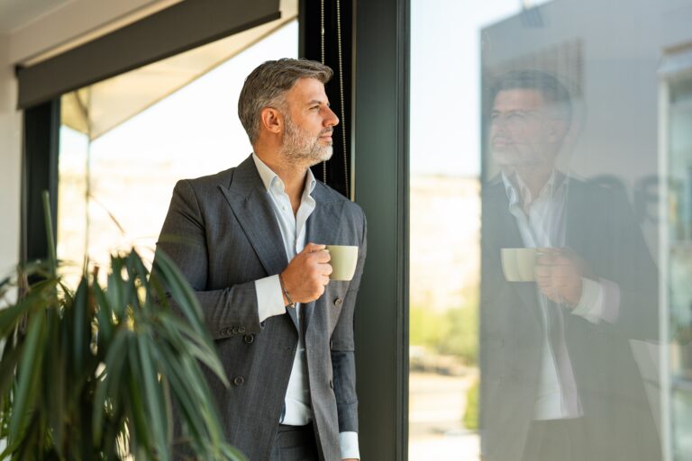 Mature businessman looking out an office window while holding a coffee cup